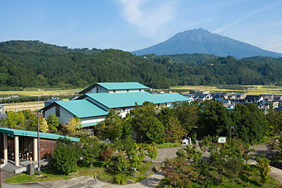 山や森に囲まれている水色の屋根の建物の写真