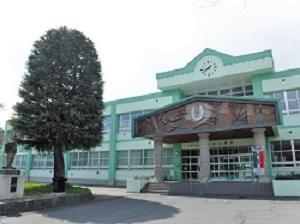 入り口付近に木の生えた、薄緑色の壁と緑色の屋根からなる小学校の正面の写真