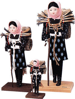 桃色の頭巾を被り、着物を着て炭を背負った女性の人形が、大、中、小の大きさで3つ並んでいる写真
