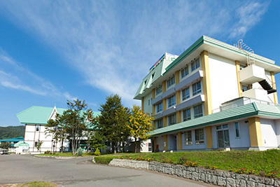 青空を背景に、薄緑色の屋根に黄色の柱と白い壁が使われた宿泊施設の写真